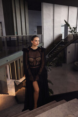 beautiful woman with dark hai in elegant black dress posing in luxury hotel hall