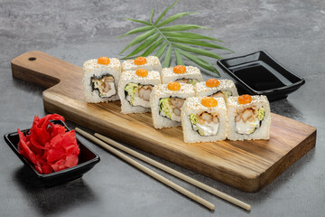 Rolls in white sesame seeds, with squid, green salad and cream sauce on a wooden board on a gray background, ginger, soy sauce and bamboo sticks. Top and side view. Photo