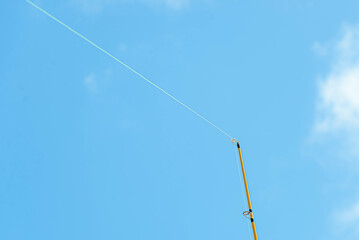 Caña de pescar tensada esperando a pescar con un cielo celeste y despejado de fondo.