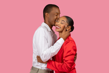 Black man kissing woman's cheek, both smiling, pink background