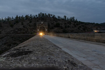 Night photography on the Roman bridge of Alcántara. A car approaching lighting up. An authentic...