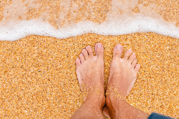 Top view of male legs in blue shorts on golden sand in sunlight. Looking down at a man in shorts standing on the sea sandy beach