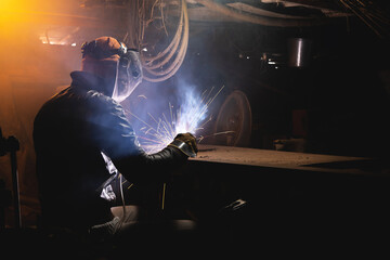 welder in a workshop welds a metal part. General plan of an old cluttered garage where a man in...