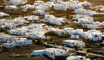 Fototapeta premium White buildings, town among volcanic black mountains and lava formations in Lanzarote, Canary Islands.