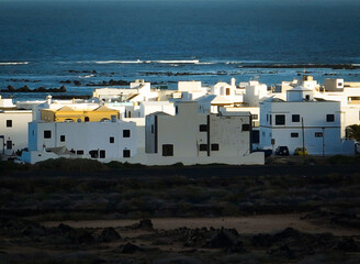 White buildings, town among volcanic black mountains and lava formations with an ocean on the background.
