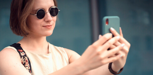 Young girl in a stylish glasses holds a mobile phone in her hands.