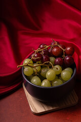 Red and green grapes served in a bowl with elegant red textile