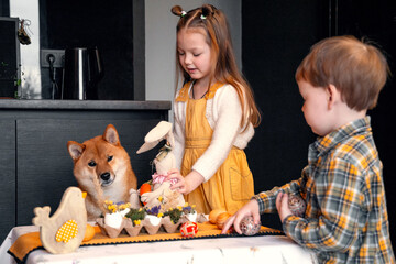 Cute and funny puppy, children cuddling. A girl and a boy sitting at the table, preparing for...