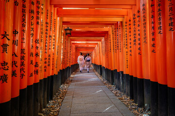 Women in traditional Japanese kimonos walk through the red torii gates at Fushimi Inari shrine in Kyoto, Japan.