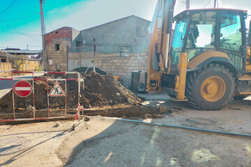 The process of repair and restoration of the operability of the underground utilities section. Excavator dug trench over pipes, workplace fenced with road signs, replacement, renewal