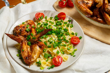Farfalle pasta with grilled chicken wings on a white plate on a salad garnished with cherry tomatoes and green onions.