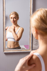 A young woman makes a face self-massage for the effect of lifting and rejuvenation while looking in the mirror
