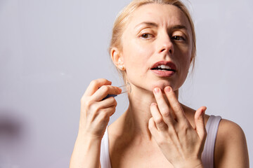 A young woman makes a face self-massage for the effect of lifting and rejuvenation while looking in...