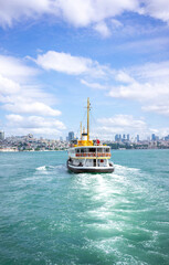 Obraz premium A classic ferry boat cuts through the turquoise waters, connecting the vibrant cityscape under a sky dotted with fluffy clouds