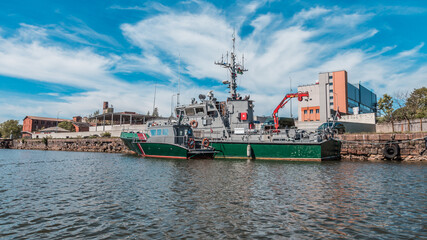 Naval patrol boat moored at the city dock with industrial equipment on board against a backdrop of...