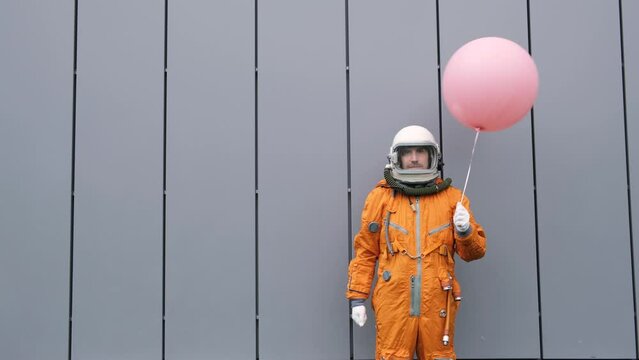 Astronaut wearing space suit with helmet holding helium balloon outdoors. Surreal concept