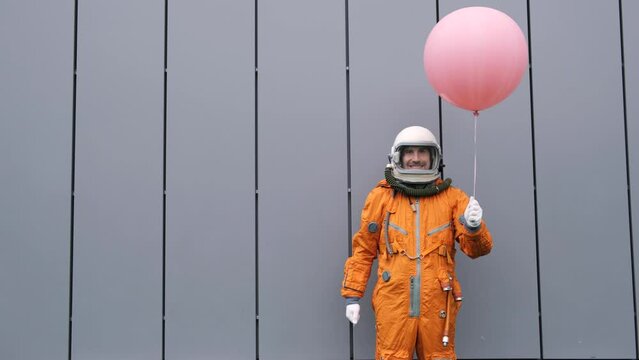 Happy astronaut wearing space suit with helmet holding helium balloon outdoors
