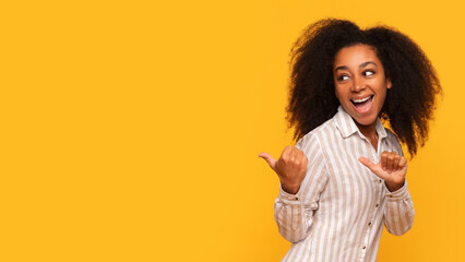 Excited black woman gesturing thumbs up at free space on yellow backdrop