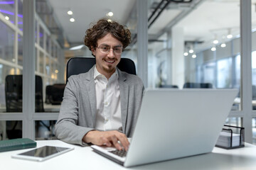 Young, professional male office worker with curly hair typing on a laptop, exhibiting efficiency...