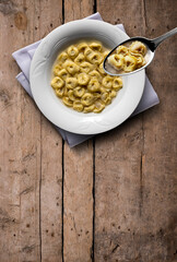 Soup plate with tortellini in broth on wooden table