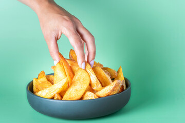 A woman's hand takes several Spanish patatas bravas from a bowl against a green backdrop. Enjoying traditional Spanish cuisine in a vibrant setting. High quality photo