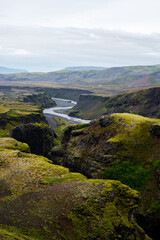 The picturesque canyon and river along a famous Laugavegur hiking trail. Amazing Icelandic landscape of volcanic mountains and river in cloudy weather with green grass and moss. Iceland in august.