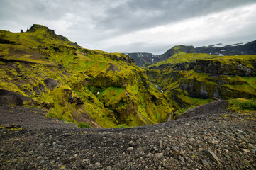The picturesque canyon and river along a famous Laugavegur hiking trail. Amazing Icelandic landscape of volcanic mountains and river in cloudy weather with green grass and moss. Iceland in august. 