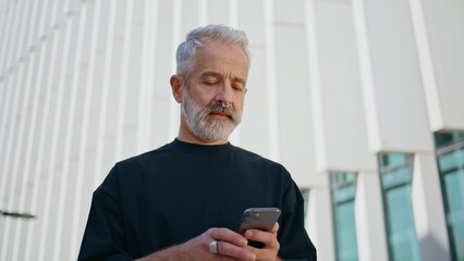 Stylish senior texting mobile phone on street. Focused mature businessman surf