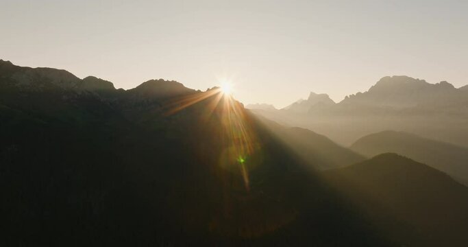 mountains dolomites italy alps bright sunrise at dawn from behind mountain peaks summer against blue sky aerial view lens flares. grandeur of mountain range. travel tourism concept