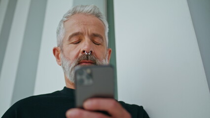 Bearded senior using mobile phone closeup. Confident brutal man wearing piercing