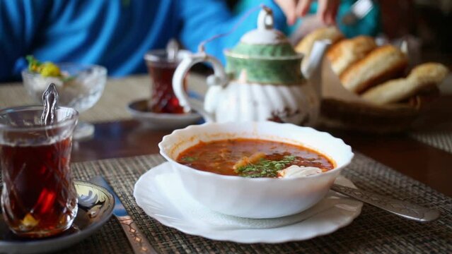 Plate of borsch, tea in glasses, teapot and buns on table at cafe.