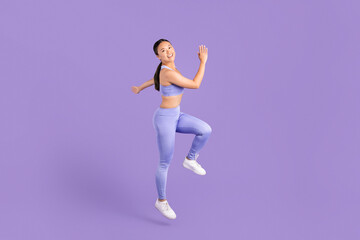 Fototapeta na wymiar Joyful asian woman in activewear running in place on purple backdrop