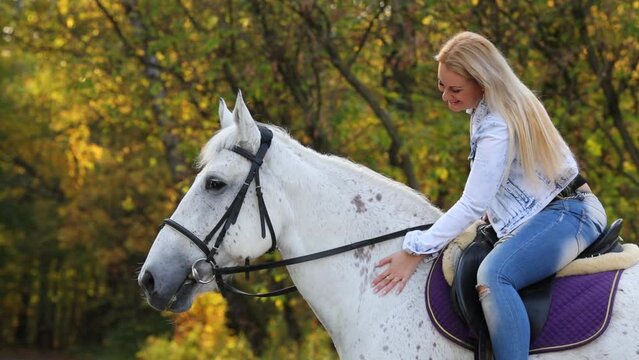 Woman with white hair sits on white horse and smiles