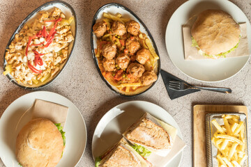 Top-down view of a table laden with diverse dishes, potatoes, burgers, chicken, sandwiches, and more. A tempting spread offering culinary variety and indulgence. High quality photo