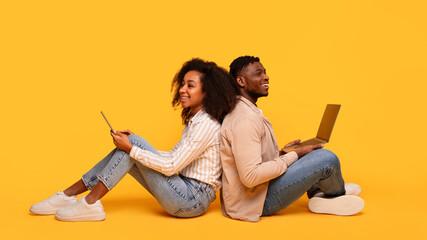 Back-to-back black couple with gadgets on yellow background