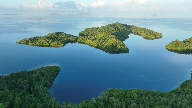 Early sunlight illuminates calm seas around the islands of Gam and Yangeffo in Raja Ampat, Indonesia. This region is mostly known for its exquisite coral reefs and overall high marine biodiversity.