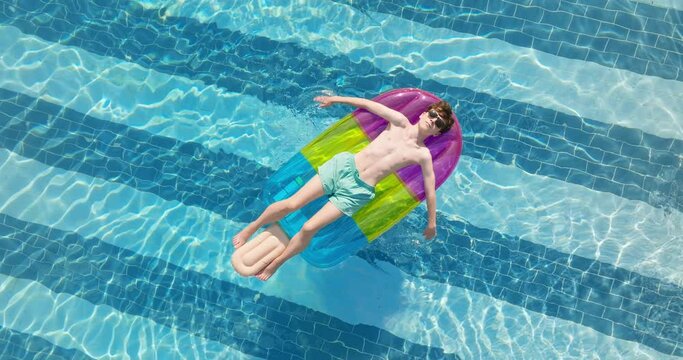 Aerial view shot relaxing young male in sunglasses in swimming pool an air ice cream in summer during an abnormally hot day in hotel on seashore in Greece. Summer holiday vacation concept. Travel tour