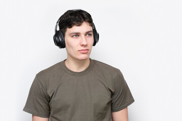 A young teenage boy in a khaki t-shirt on a light background looks away and enjoys music he listens...