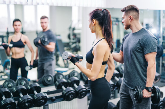 Man and Woman Exercising With Dumbbells in Gym for Strength Training and Fitness. A man and a woman are seen lifting dumbbells in a gym, focusing on strength training and improving their fitness.