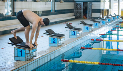 Male swimmer jumping off the starting block into the pool. Concept of determination and competitive...