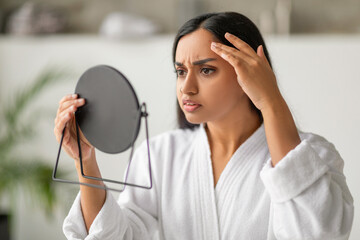 Disappointed young indian woman looking into the mirror after bath