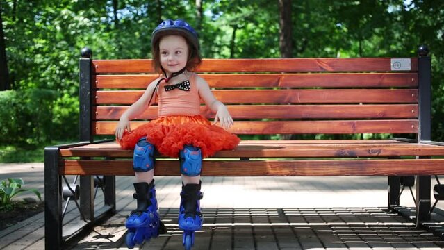 Cute little girl in blue helmet and roller skates sits on bench