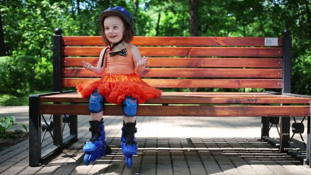 Little girl in helmet and roller skates sits on bench and haves fun