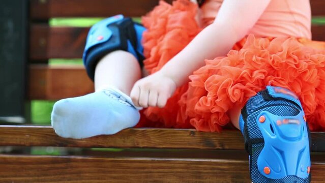 Legs of little girl sitting on bench and removing roller skates