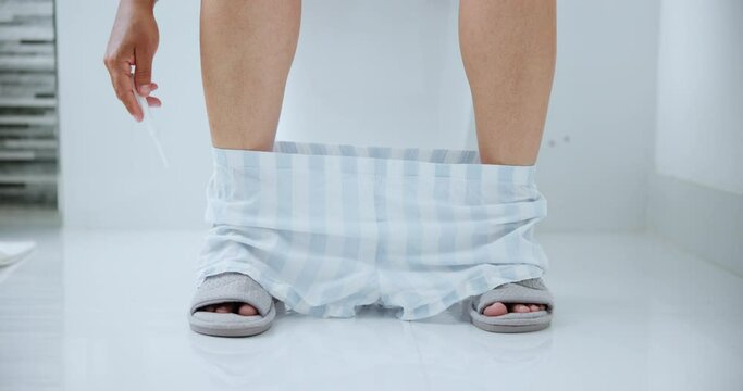 Woman, bathroom and pregnancy test with legs, waiting and hope for baby, fertility or morning. Home, pyjamas and pee on stick for result, toilet and prenatal with hand, motherhood and patience