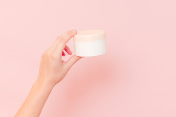 Fototapeta na wymiar Round jar of cosmetic cream in hand on pink background. Cosmetics beauty mockup for product branding