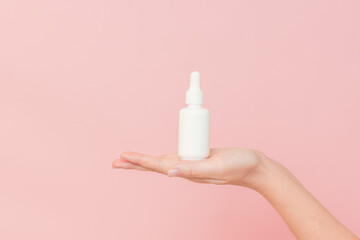 Glass cosmetic bottle for serum (hyaluronic acid and collagen) in hand on pink background. Beauty...