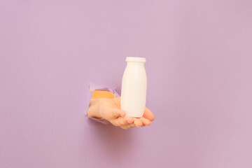 Fototapeta na wymiar White bottle of probiotic yogurt for digestive system in hand with lilac background. Dietary supplements for stomach