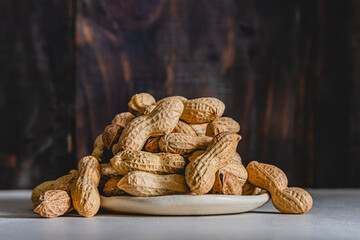 Mountain of roasted peanuts in shell on a plate and dark background