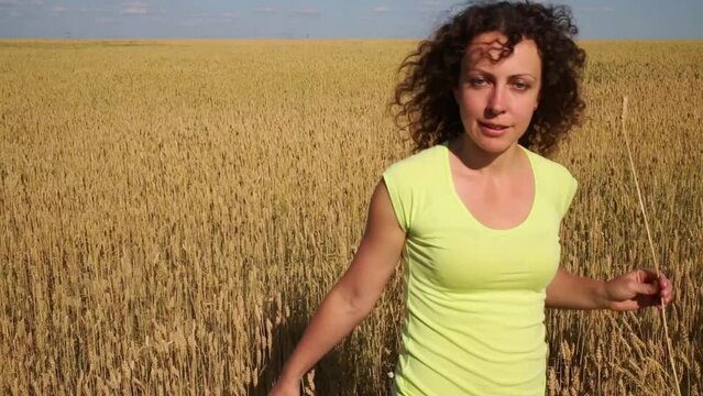 Woman in shorts goes in yellow wheat field at summer day
